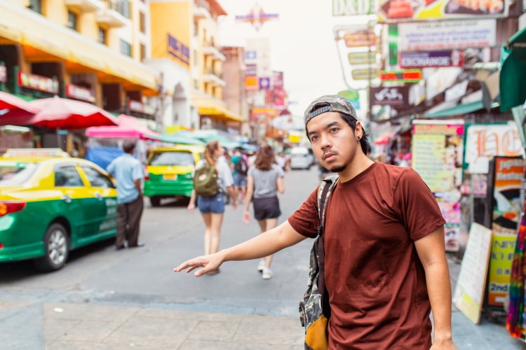 young asian man hailing a taxi on a Thailand street
