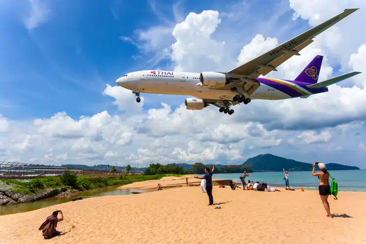 Thai Airways Plane Flying Low Over The Beach To Land At Phuket Airport In Thailand