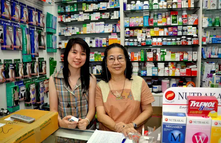 Thai Woman And Daughter Owners Of A Pharmacy In Bangkok Thailand With Medicine In The Background
