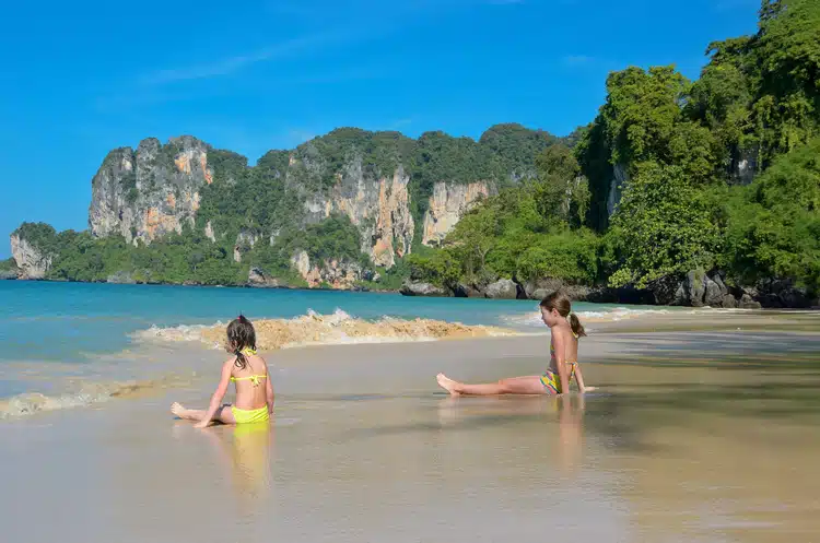 Two Young Girls Playing On A Thailand Beach With Beautiful Rock Formation Background And Sand